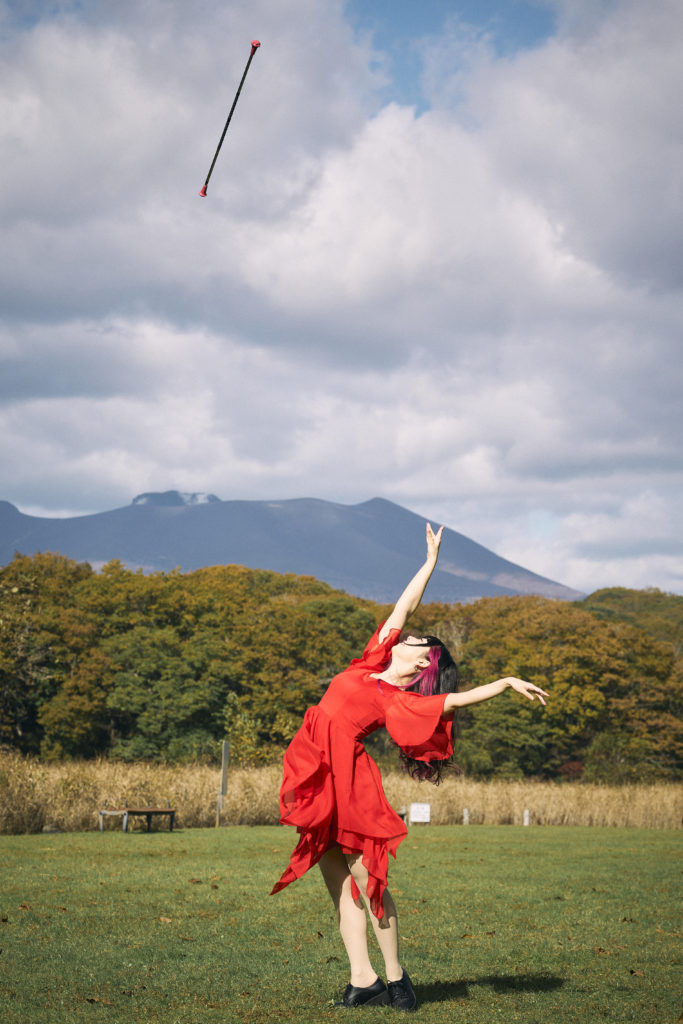バトンを空に投げている赤いドレスの女性